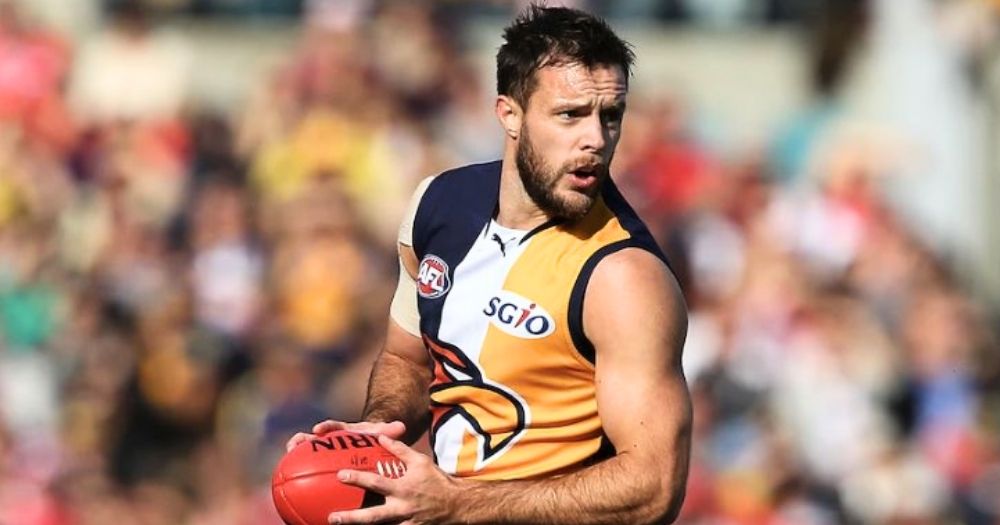 AFL player Mitch Brown, who recently came out as bisexual, holding the ball while on the field and running, with the audience in the background.