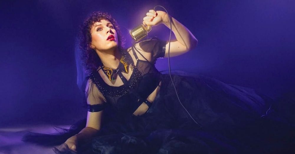 Sam Nicoresti, who became the first trans comedian to win the Edinburgh Fringe comedy award, wearing an elegant black dress and posing on the floor while holding a microphone for the poster of their show Baby Doomer.