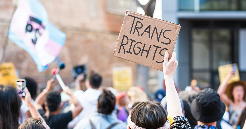 This article about the puberty blocker ban in Northern Ireland. The image shows a protest march with one person holding a sign on cardboard that says, 