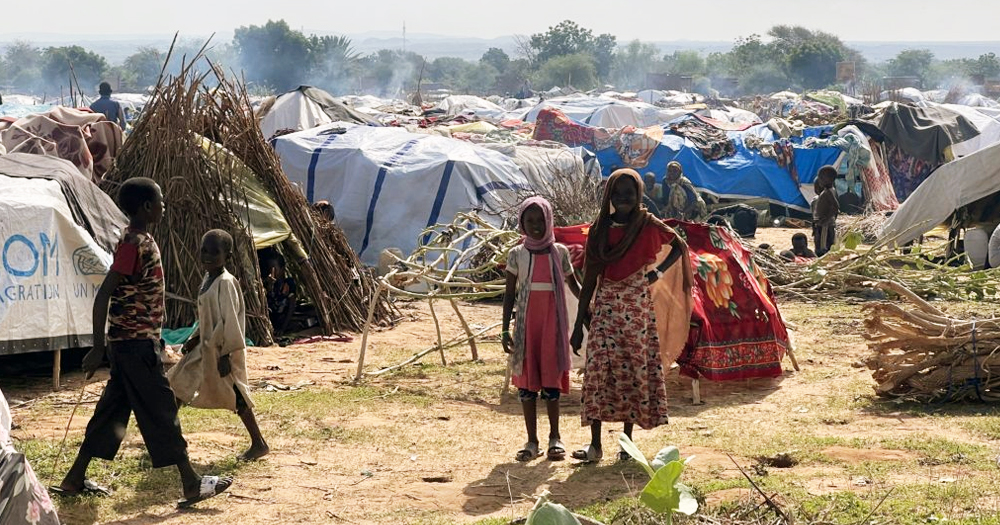 A refugee camp in Sudan, where people are facing famine, showing tents in the background and kids looking at the camera and walking.