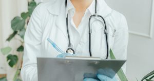This article is about Hilary Cass being appointed to review Northern Ireland's gender identity services. The image shows the torso of a doctor writing on a clipboard.