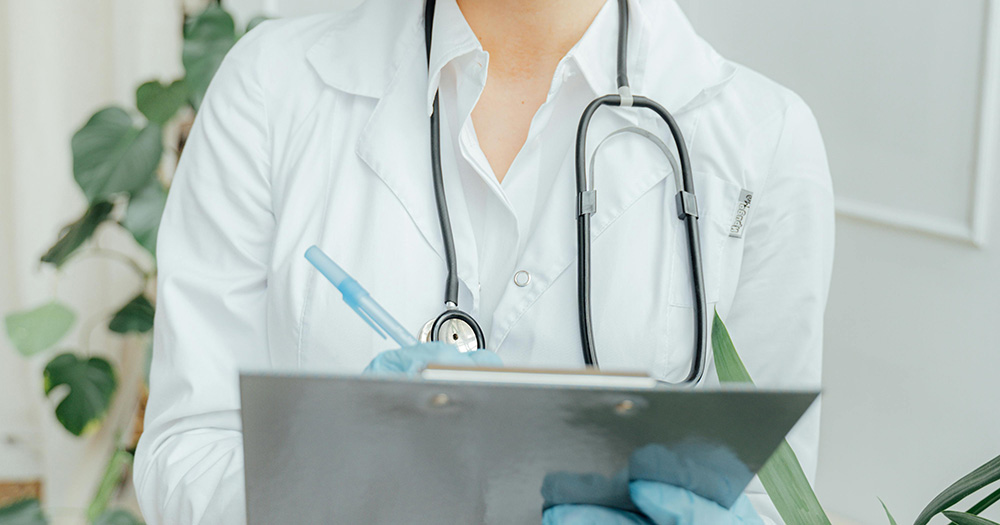 This article is about Hilary Cass being appointed to review Northern Ireland's gender identity services. The image shows the torso of a doctor writing on a clipboard.