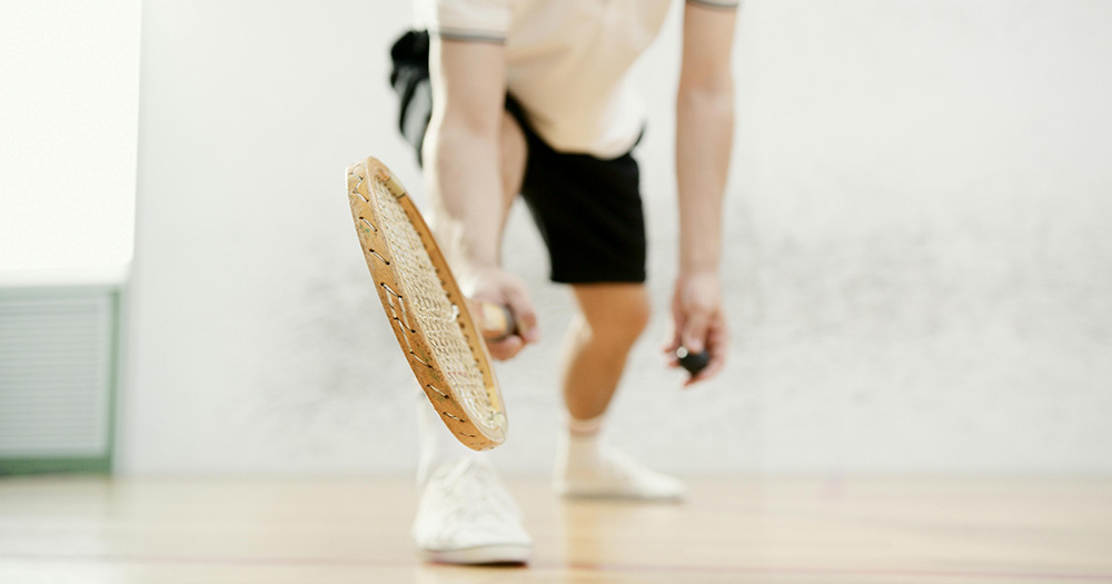 This article is about Ireland hosting the European LGBTQIA+ Squash Open. The image shows a person on a squash court getting ready to serve with a racket in their hand.