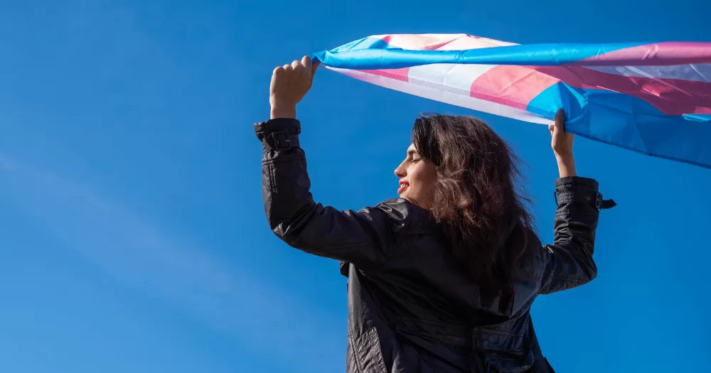 The image shows someone holding a Trans Pride flag, TENI will be holding an event to mark ten years of Gender Recognition