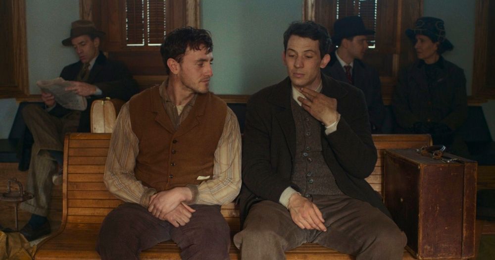 Paul Mescal and Josh O'Connor in a scene of The History of Sound, sitting on a bench as O'Connor touches his throat and Mescal looks at him.