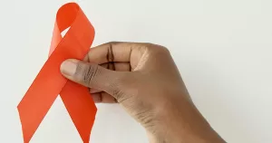 This article is about Ireland's HIV Action Plan. The image shows a hand holding a red ribbon in front of a white background.