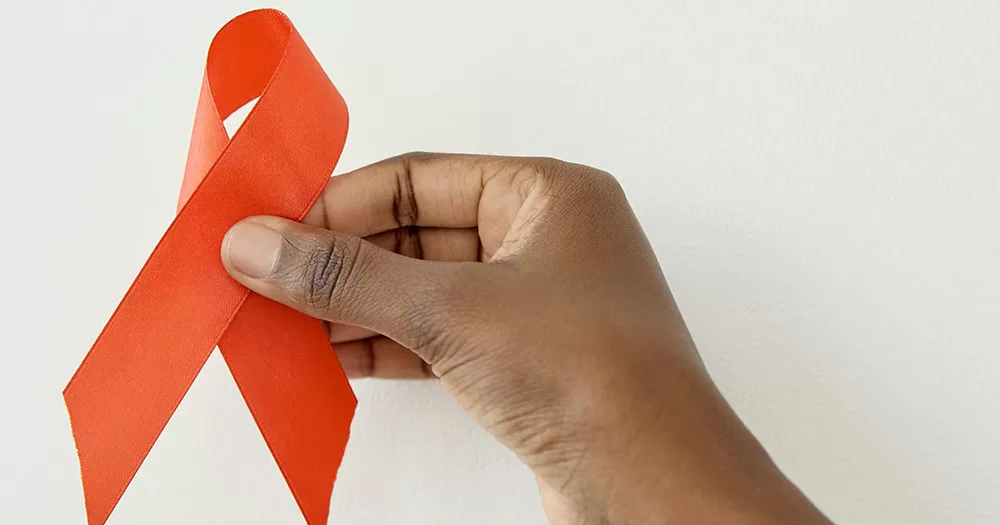 This article is about Ireland's HIV Action Plan. The image shows a hand holding a red ribbon in front of a white background.