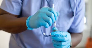 This article is about an HIV prevention injection approved in the EU. In the photo, the hands of a doctor holding a syringe and medicine while wearing latex gloves.