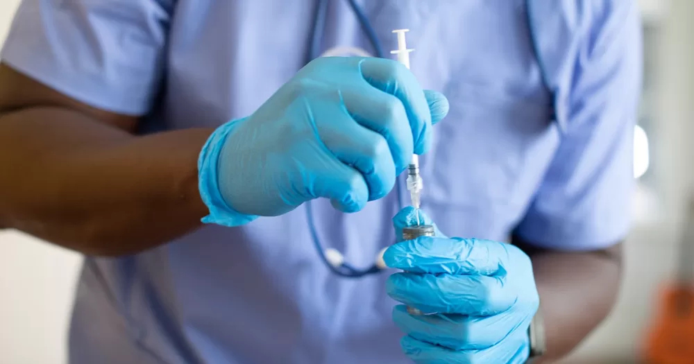 This article is about an HIV prevention injection approved in the EU. In the photo, the hands of a doctor holding a syringe and medicine while wearing latex gloves.