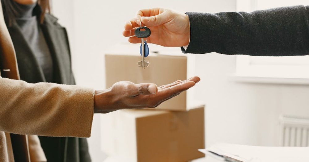 This article is about US LGBTQ+ couples buying homes in Ireland. In the photo, the hands of two people exchanging a set of keys, with a third person in the background.
