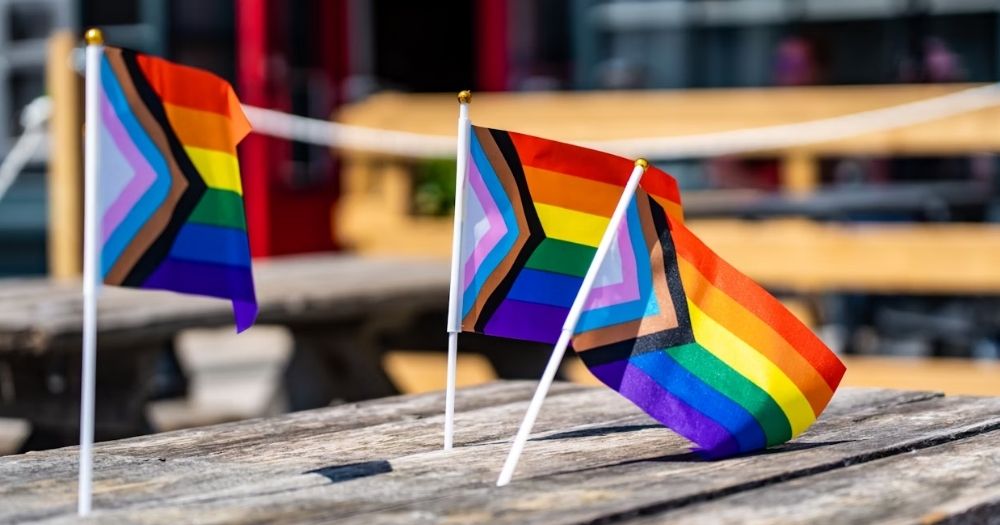 This article is about LGBTQ+ charities in Ireland. In the photo, three small progress Pride flag propped up on a wooden table.