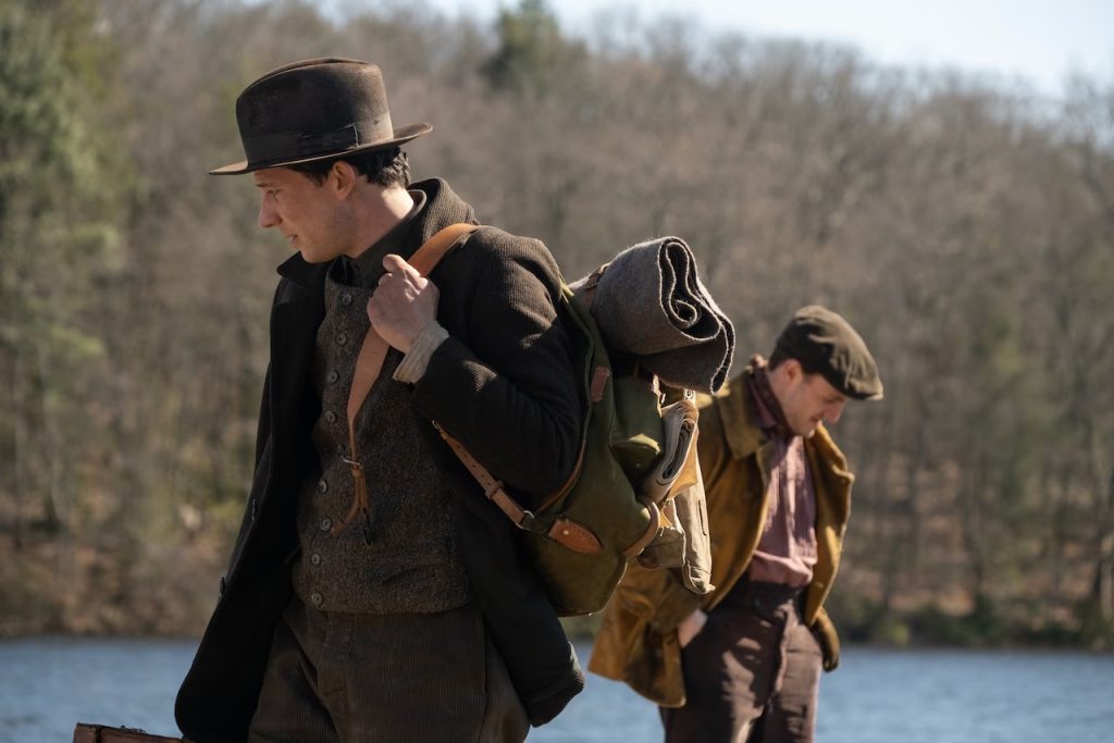 two men at a lake wearing brown coats and hats and backpacks in the early 1900s. A still from The History of Sound. Queer halloween costume ideas 2025.