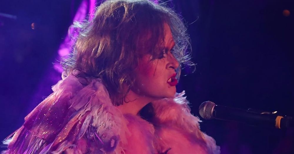 Irish artist SexyTadhg performing on stage at Electric Picnic, as they sing into a microphone while playing the piano.