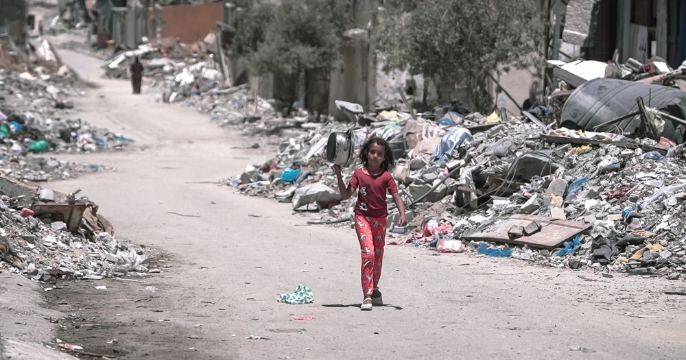 This article is about a UN inquiry that concluded Israel is committing genocide in Gaza. The image shows a girl walking through Gaza city with a pot in her hand.