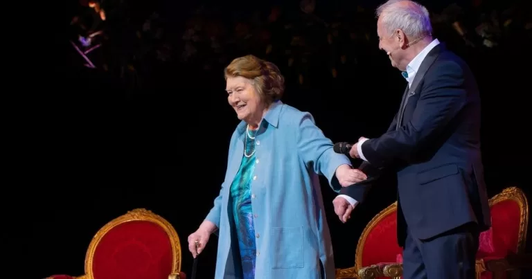 Patricia Routledge, who played. Hyacinth Bucket, is welcomed onto stage by a man on her left.