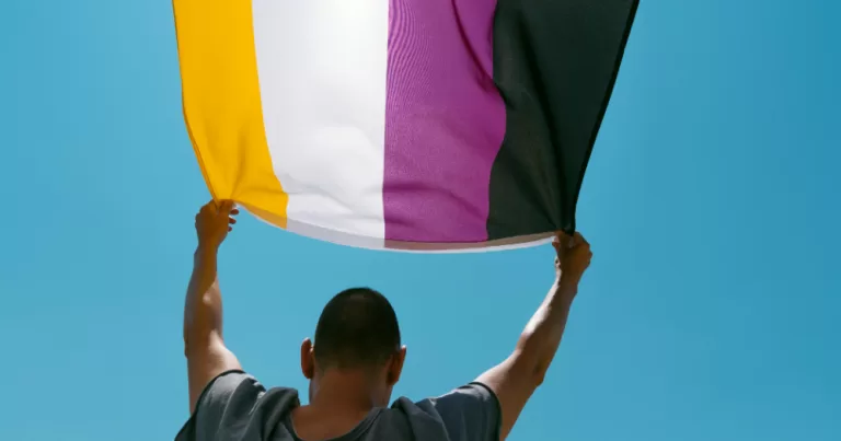 A person holds a Non-binary flag. This article covers research on sexuality, sexual health, and relationship satisfaction among non-binary people.