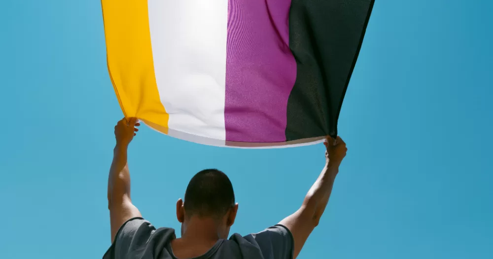 A person holds a Non-binary flag. This article covers research on sexuality, sexual health, and relationship satisfaction among non-binary people.