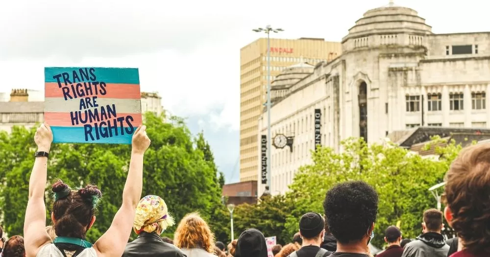 Trans activists gather at a protest. One holds a sign that says 