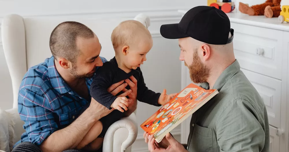 This article is about Irish surrogacy law. In the photo, two dads holding a baby and showing them a book.