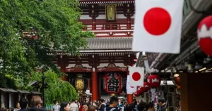 This article is about Japan increasing protections for same-sex couples. In the photo, small Japan flags flying on a historic building with people walking around.