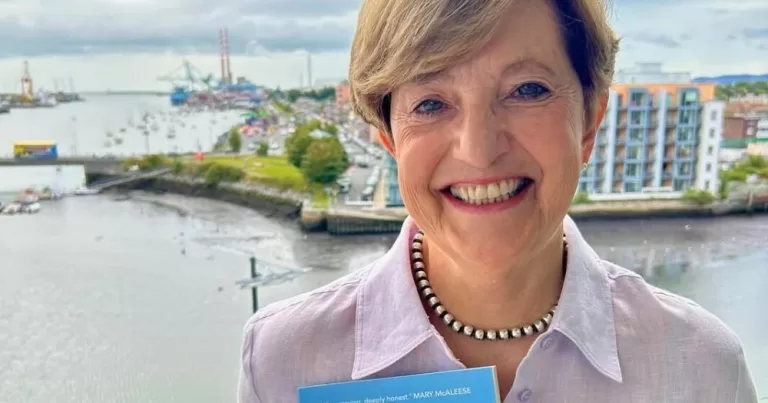 Katherine Zappone smiling at the camera while holding up her new memoir.