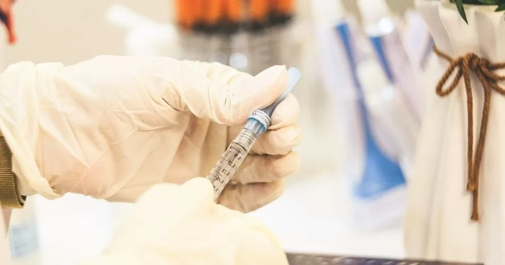 A hand wearing medical gloves holds an injection.
