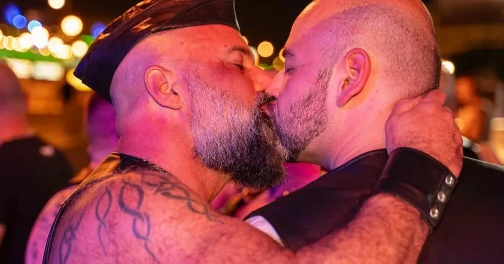 Image shows two men with leather accessories kissing.