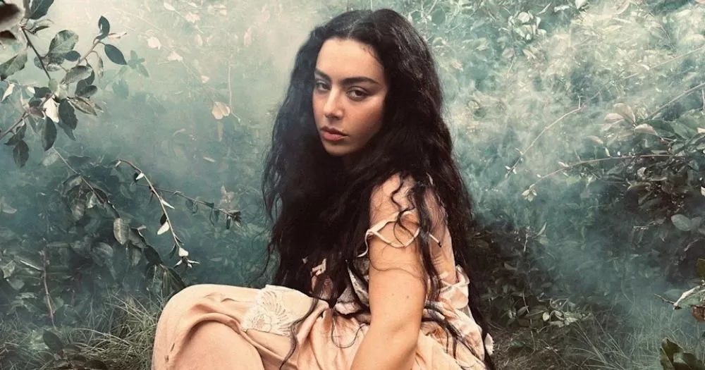 Charli XCX releases 'Chains of Love'. Charli sits with long flowing curly black hair amidst a foggy forest scene.