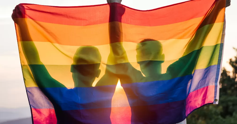 Two people hold up a Pride flag - this article covers words reclaimed by the LGBTQ+ community