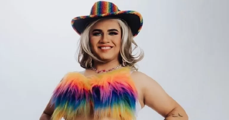 Image shows drag queen Hilary Rivers who was detained by ICE this year. She ie wearing a rainbow coloured hat and a fluffy rainbow coloured bra.