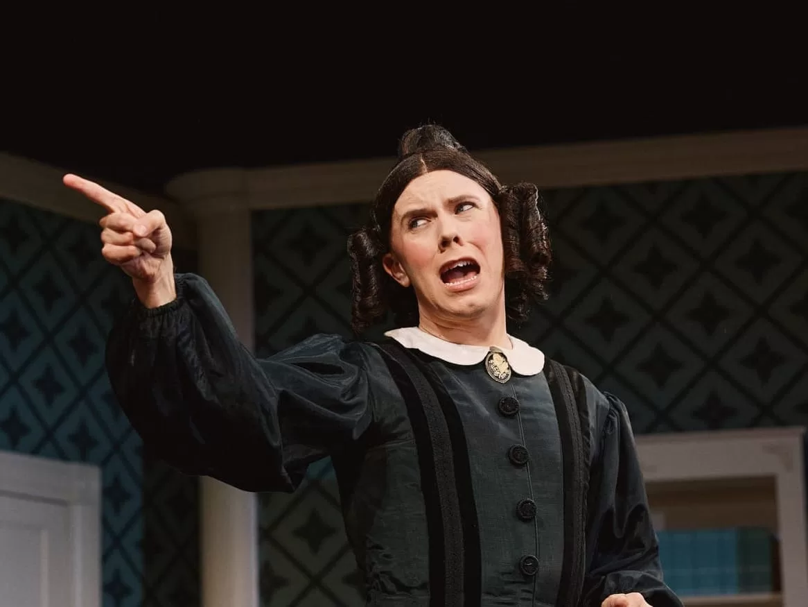 Cole Escola on stage as Mary Todd Lincoln, in a curly brunette wig.