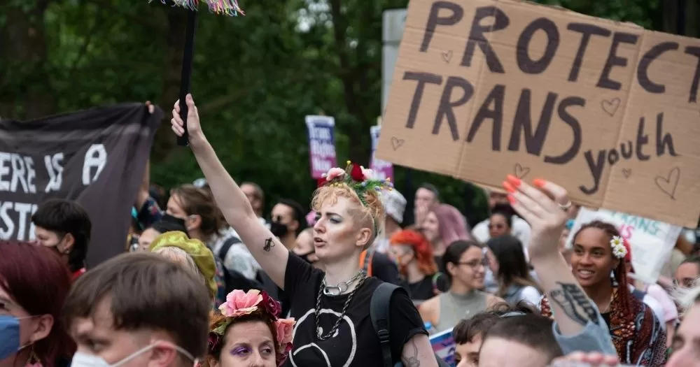 Protestors at a rally hold signs supporting trans youth. This image is being used to accompany an article on a ban on puberty blockers in New Zealand.