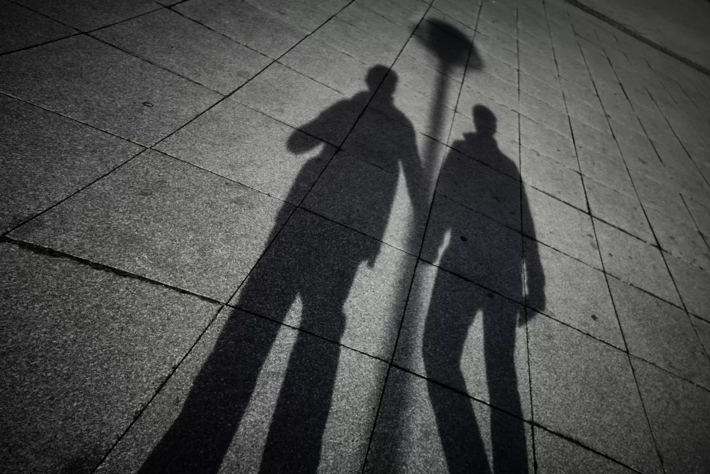 Image shows the shadows of two men holding hands. This image is being used to represent the concept of outing in the LGBTQ+ community.