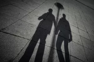 Image shows the shadows of two men holding hands. This image is being used to represent the concept of outing in the LGBTQ+ community.