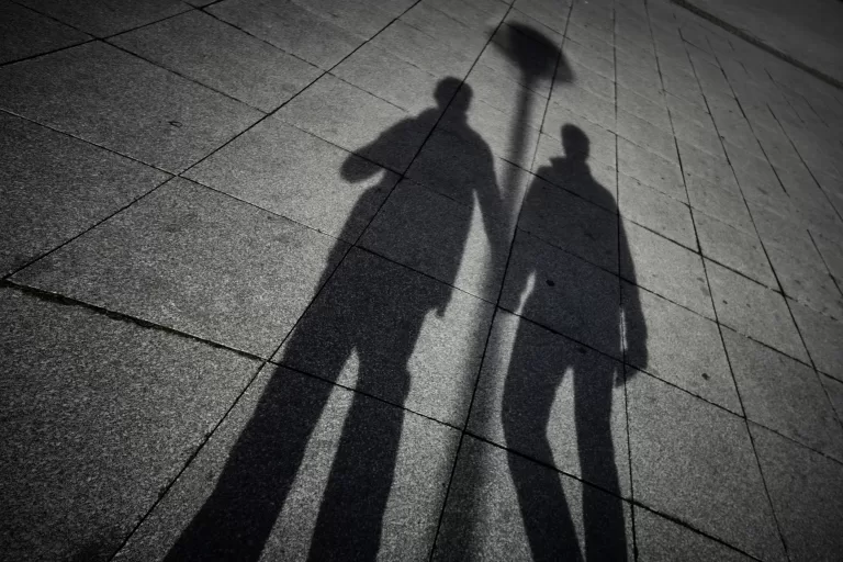 Image shows the shadows of two men holding hands. This image is being used to represent the concept of outing in the LGBTQ+ community.