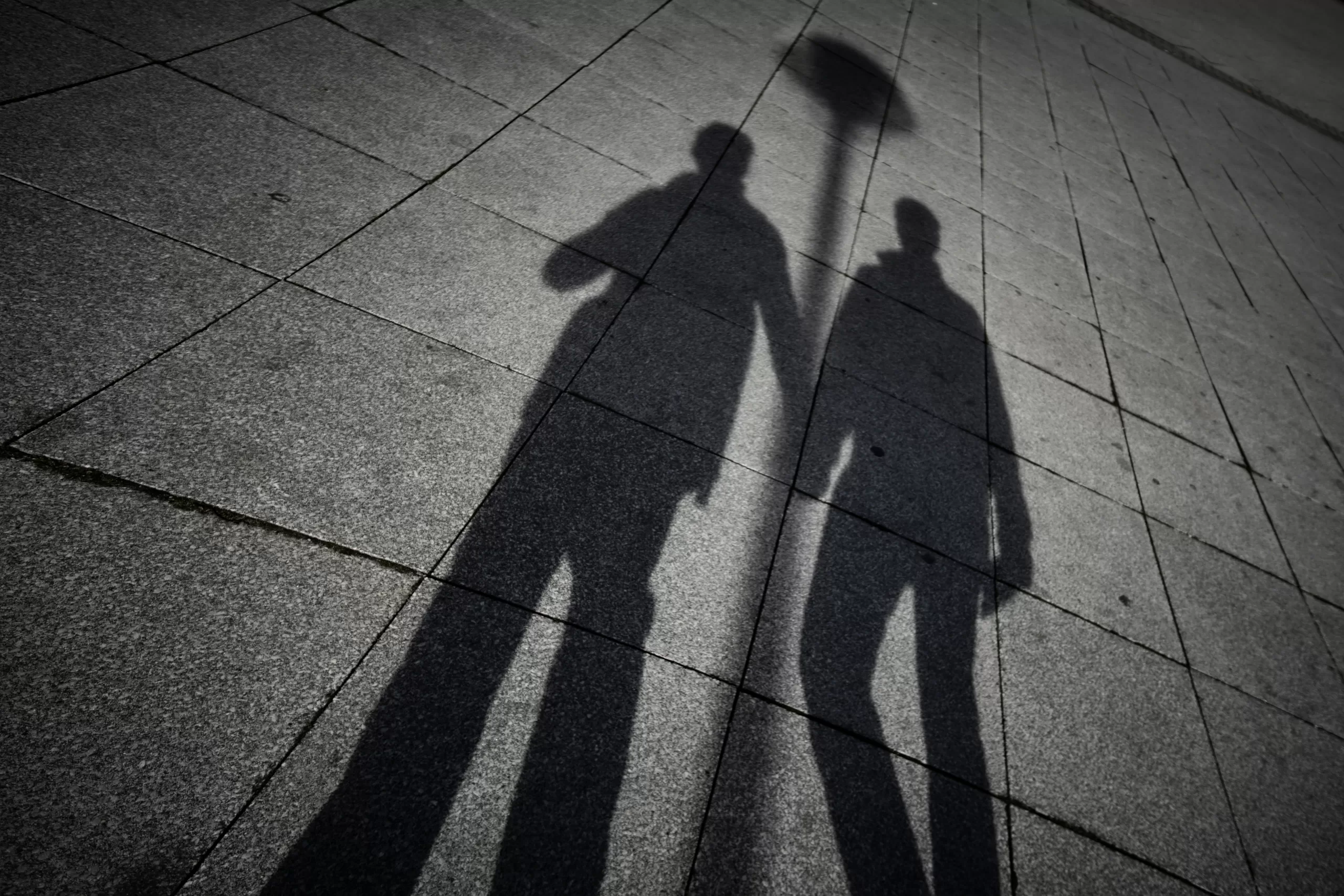Image shows the shadows of two men holding hands. This image is being used to represent the concept of outing in the LGBTQ+ community.