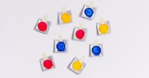 Trans and non-binary birth control. Colourful condom packets taped to a white wall.