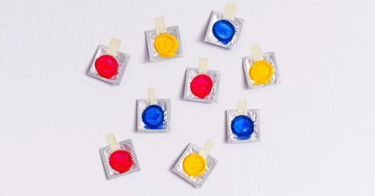 Trans and non-binary birth control. Colourful condom packets taped to a white wall.