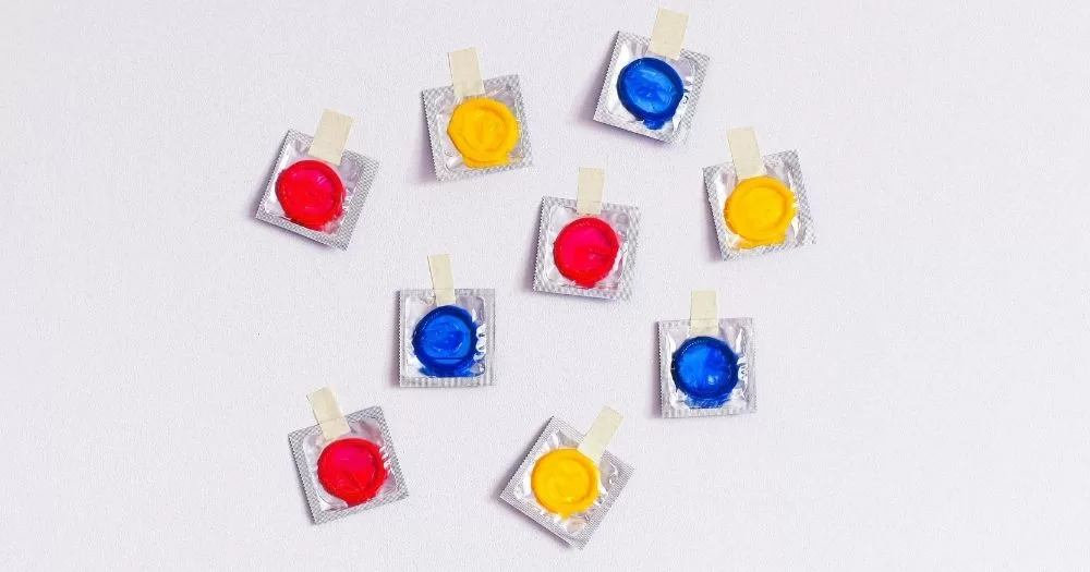 Trans and non-binary birth control. Colourful condom packets taped to a white wall.