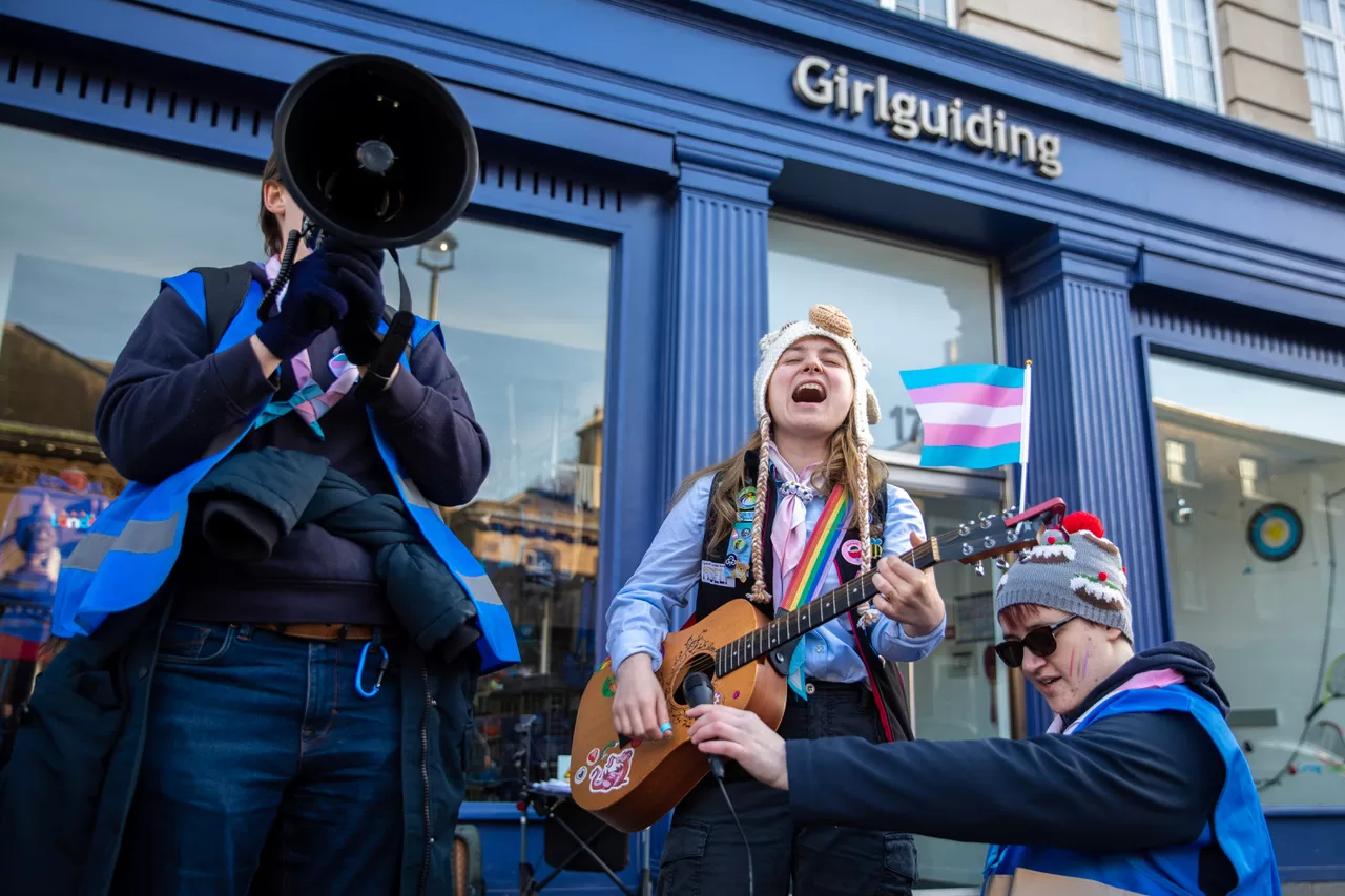 A protestor holds a megaphone, while another plays guitar outside Girlguiding HQ.