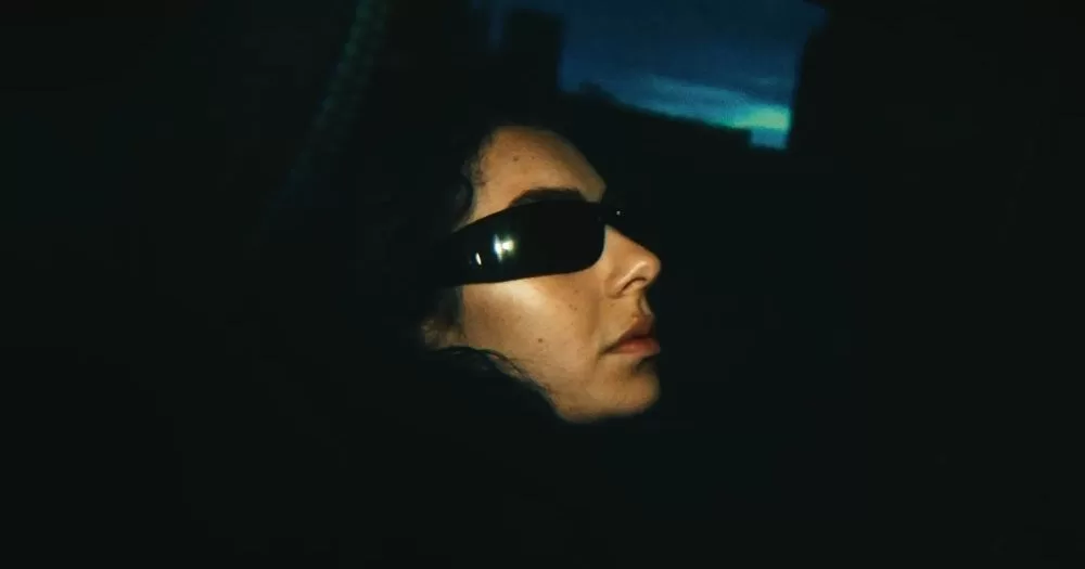 Trailer released for Charli XCX and A24's The Moment. A portrait of Charli with her signature sunglasses on in a dark abyss.