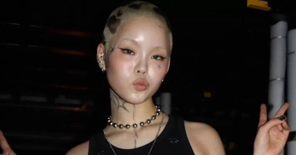 Jpop rapper and XG member Cocona, who recently came out as transmasc non-binary, posing for a picture making a peace sign with her hand.