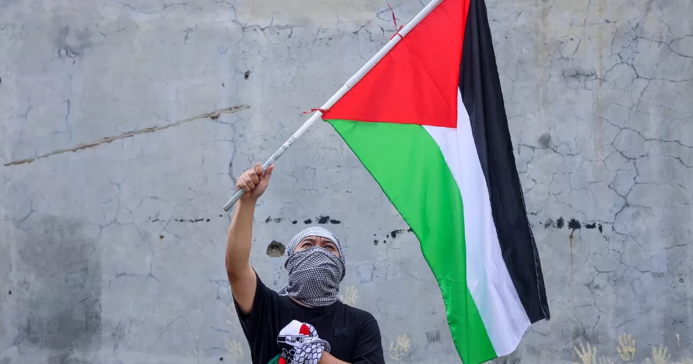 A person holding a Palestinian flag. The Freedom Theatre has announced they will perform in Ireland