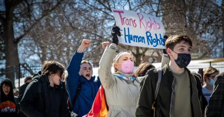 This article is about warnings that a single-sex spaces guidance could impact trans people's mental health. In the photo, people protesting and marching with a sign that reads "Trans rights are human rights".