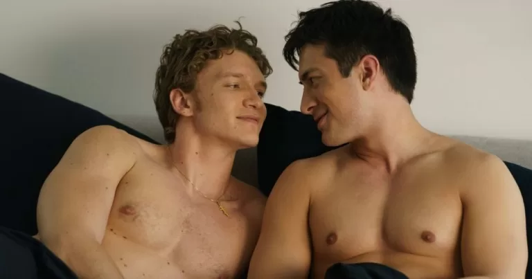 Heated Rivalry is finally coming to Ireland. The image shows Connor Storie and Hudson Williams gazing lovingly at each other while shirtless in bed.