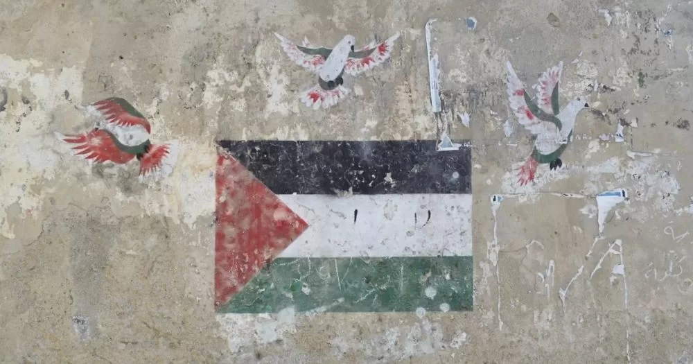 This article is about queer history of Palestine. In the photo, a Palestinian flag painted on a wall with some birds.