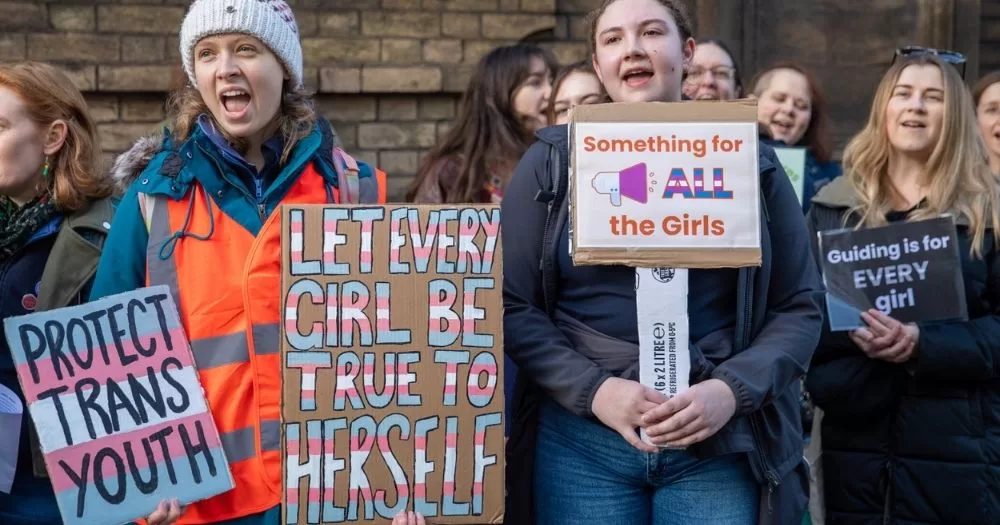 Protestors hold signs that say Protect Trans Youth, Let Every Girl Be True to Herself and Something for All the Girls while protesting for trans inclsusion in the Girl Guides.