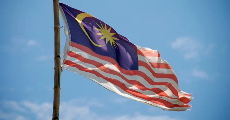 A Malaysia flag with red and white stripes and a blue rectangle with a moon and sun.