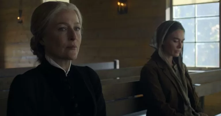 The image shows The Abandons stars Gillian Anderson and Lena Headey, in a still from the series. They are seated a distance apart on what appears to be a church pew, with Anderson on the left, wearing a black shirt with her hair in a bun, staring straight ahead. Headey is dressed in brown, with a shawl covering her head, and her eyes on the floor.