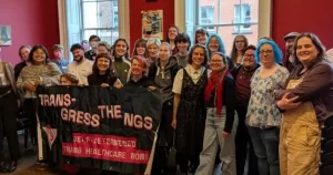 Transgress the NGS stand together holding a sign.